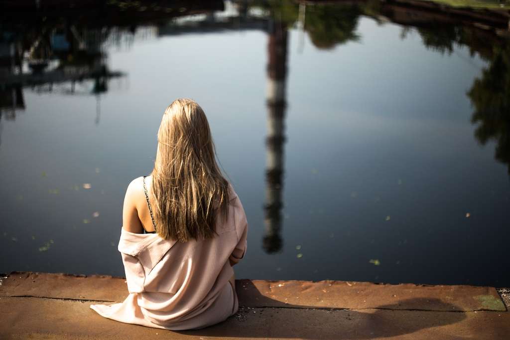 blond girl sitting on dock by lake