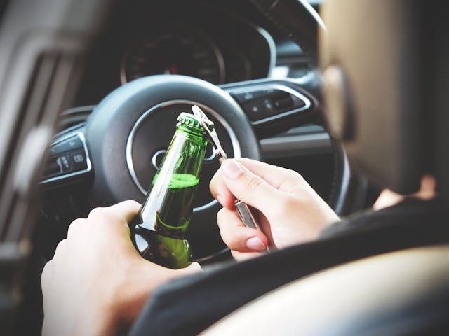 Drunk driver opening a bottle of beer behind the wheel