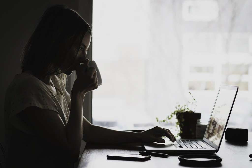 woman drinking coffee doing research on laptop