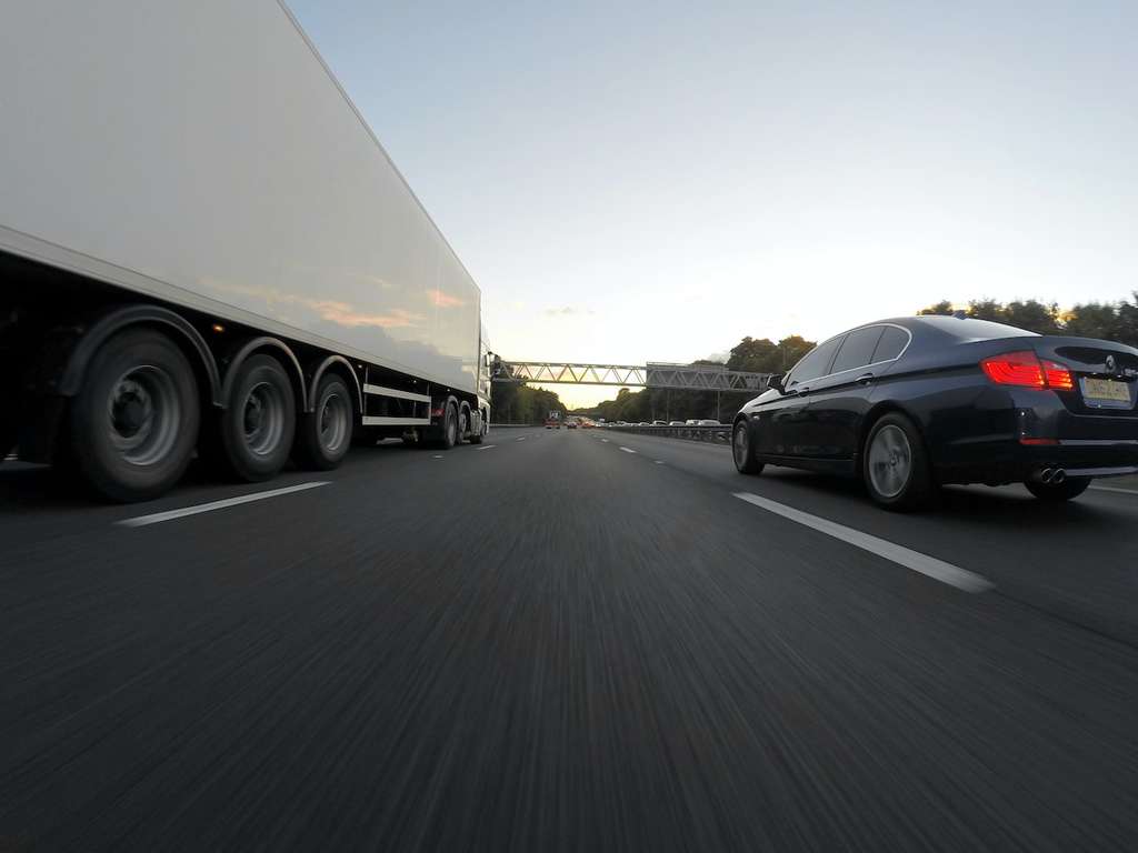 A freight truck running beside a sedan on a highway