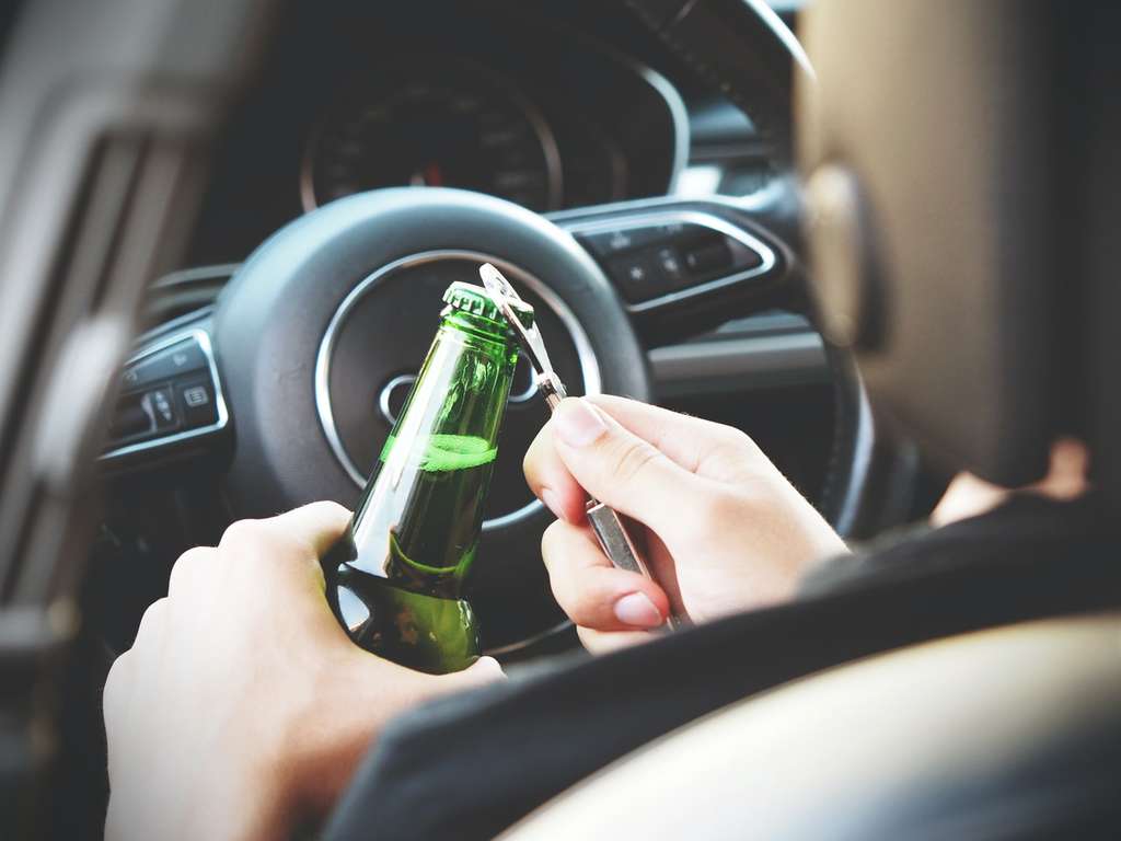 Person opening beer bottle behind the wheel of a car