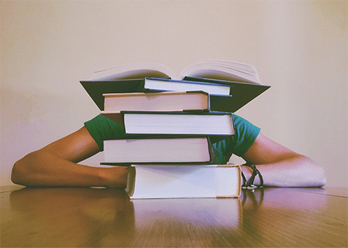 student hiding behind pile of books